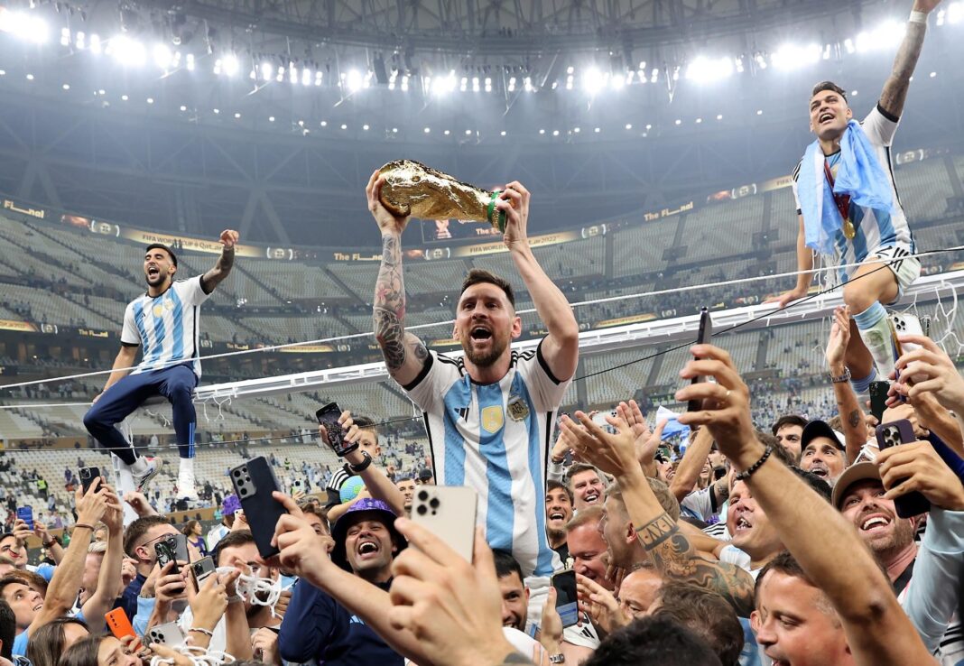 Grupo de personas con camisetas de la selección argentina observando un partido en una pantalla, representando la expectativa por el Mundial 2026.