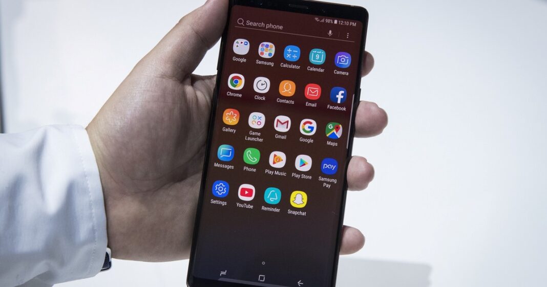 Persona sosteniendo un teléfono celular con un símbolo de alerta y un candado en la pantalla, representando la seguridad del dispositivo.