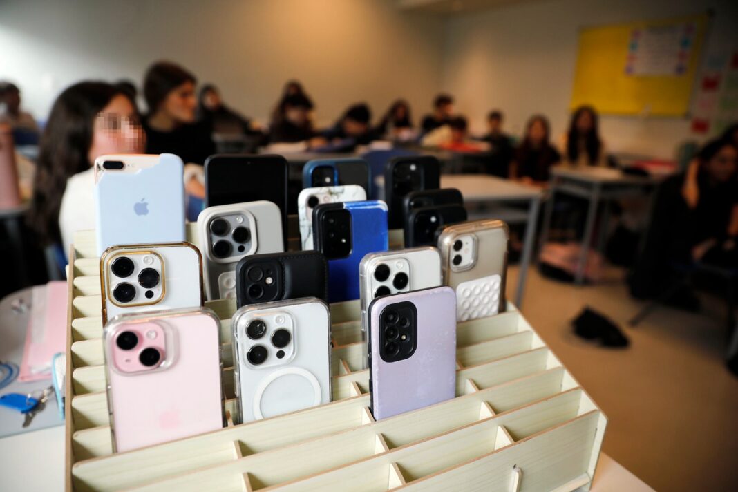 Estudiantes en un aula con celulares sobre el escritorio, ilustrando la regulación de dispositivos en escuelas según informe de Unesco